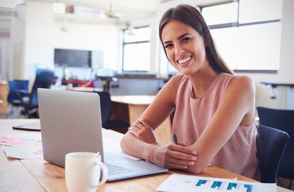 Lächelnde Mitarbeiterin am  Laptop mit Kaffeebecher